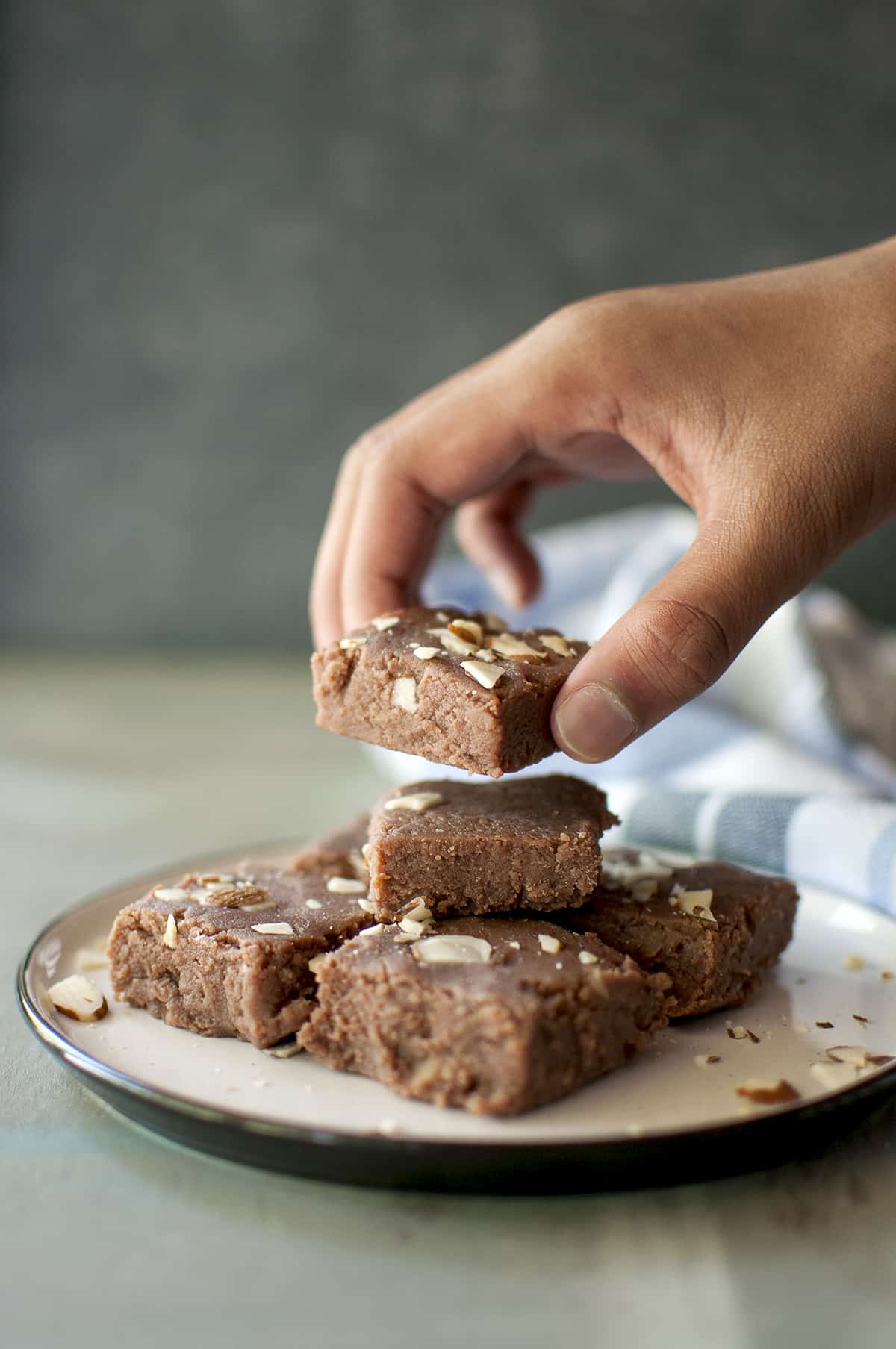 Hand picking up chocolate barfi from a grey plate