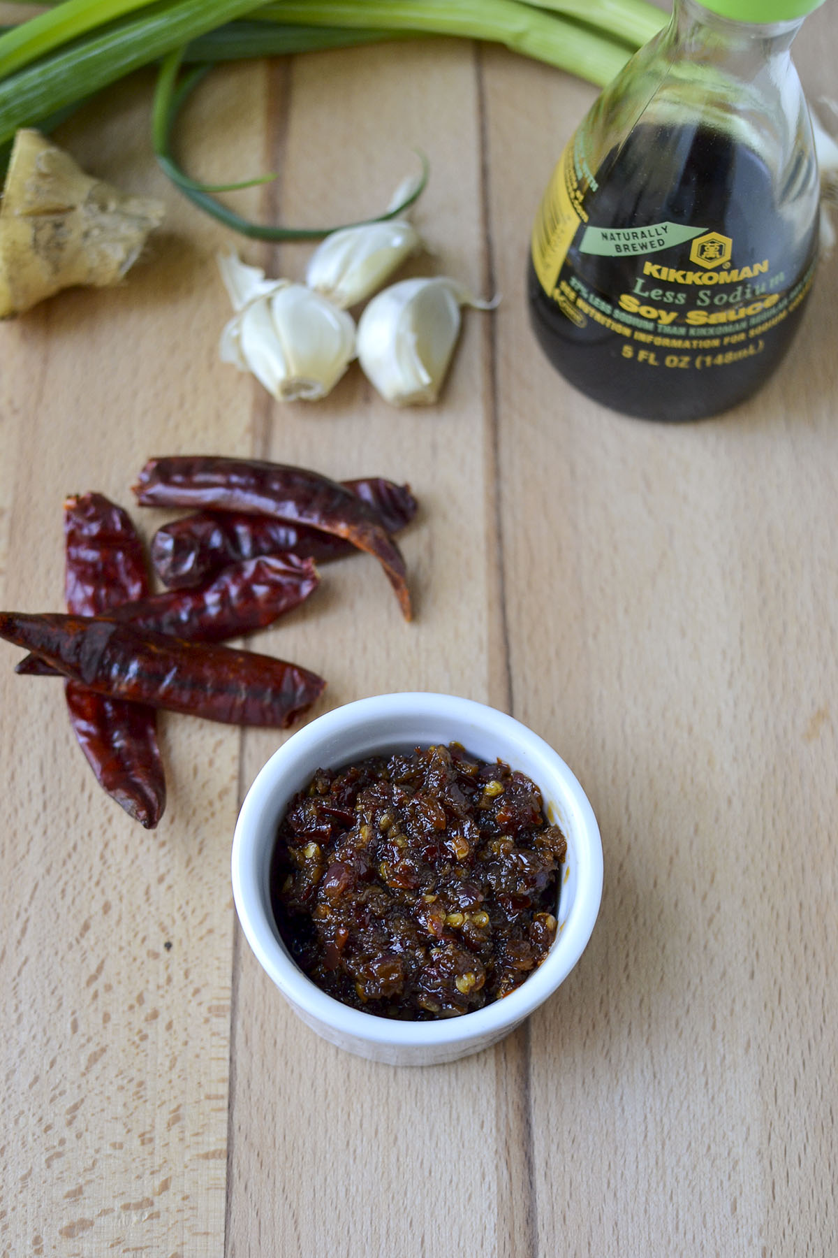 White bowl with Indo-Chinese Chili-garlic sauce with red chiles, ginger, garlic and soy sauce in the background