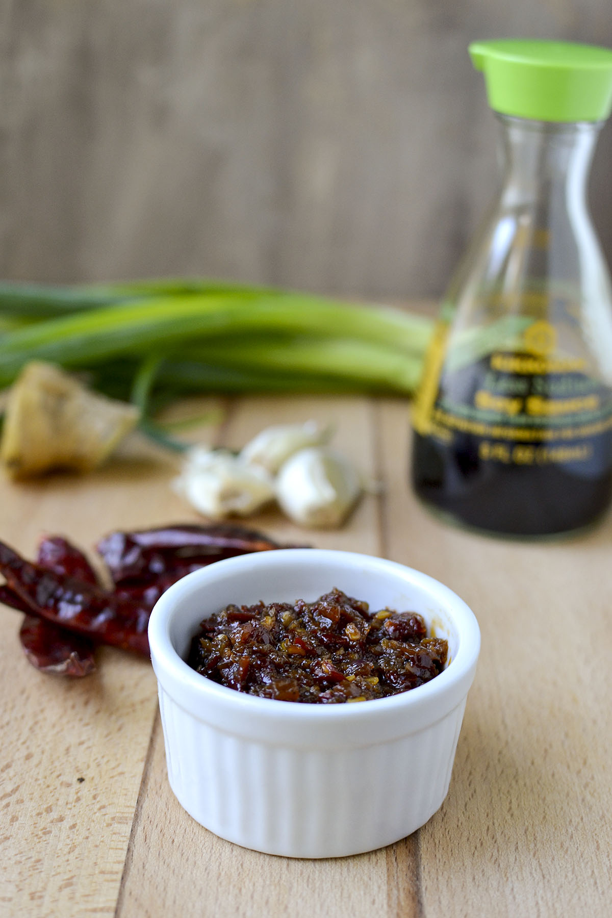 White bowl with Schezwan Chili Sauce with dry red chilies, garlic and soy sauce in the background