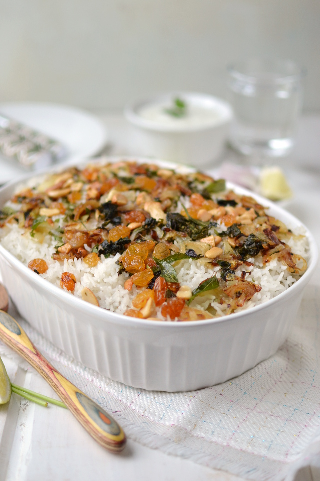 White baking pan with rice topped with nuts, raisins and herbs