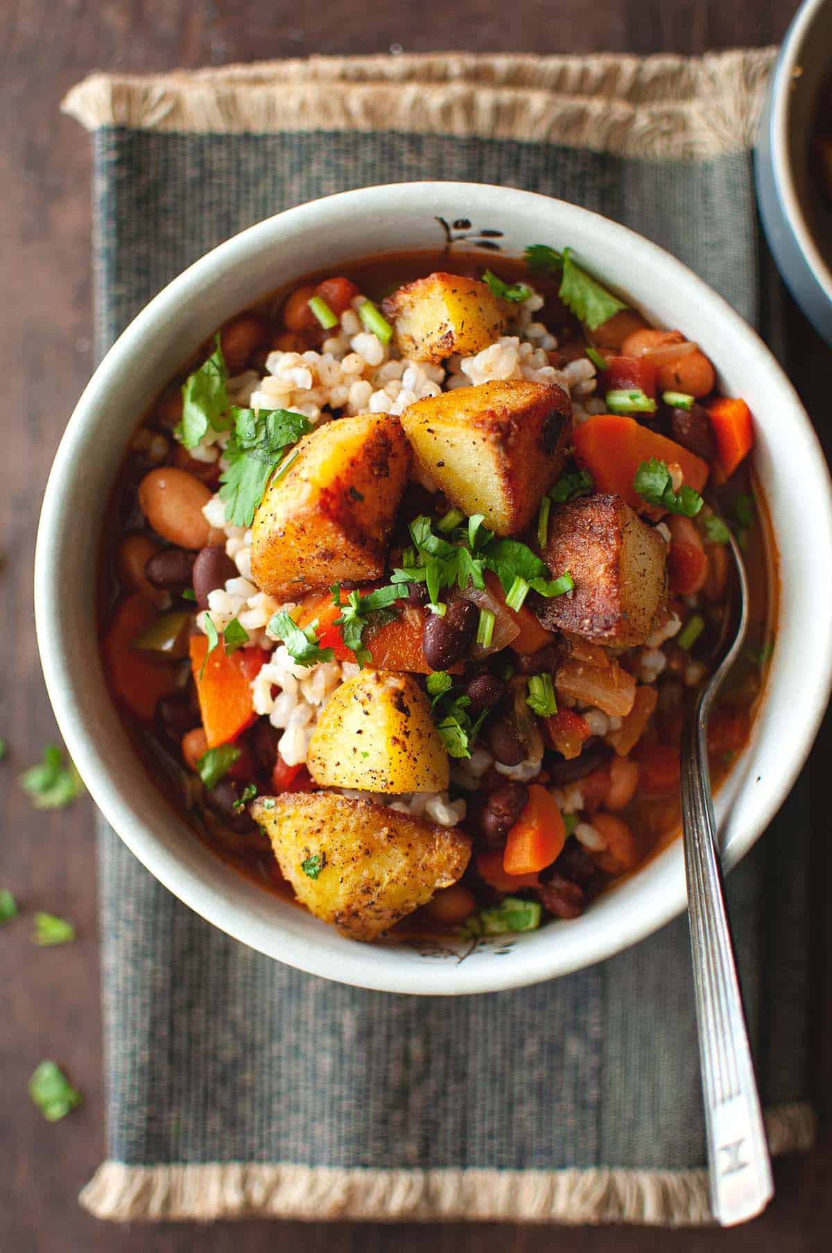 White bowl with veggie stew topped with roasted potatoes.