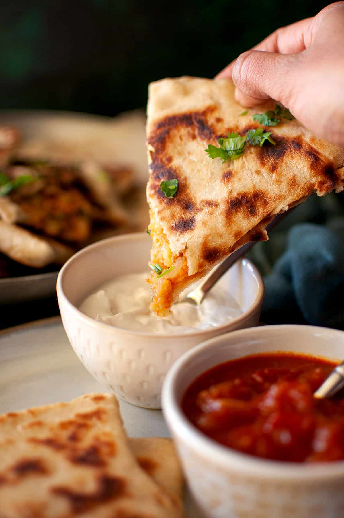 Hand dipping piece of Afghan bread in yogurt.