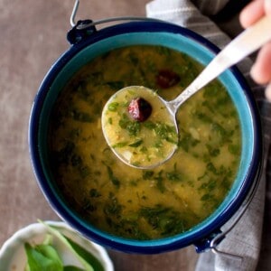 Hand holding a spoon with methi moong dal rasam