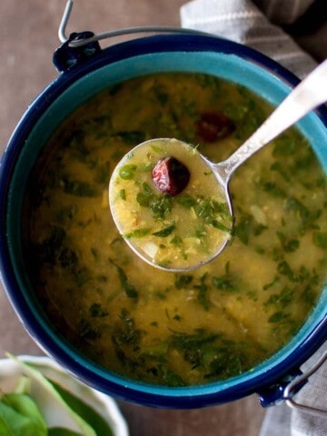 Hand holding a spoon with methi moong dal rasam