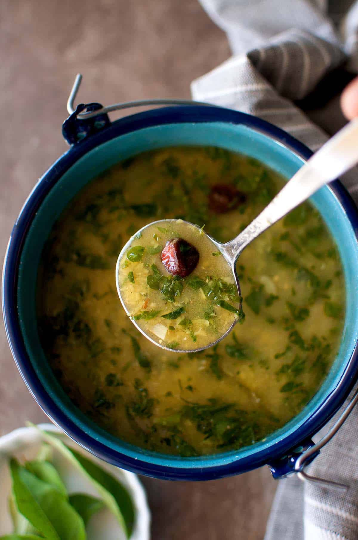 Hand holding a spoon with methi moong dal rasam