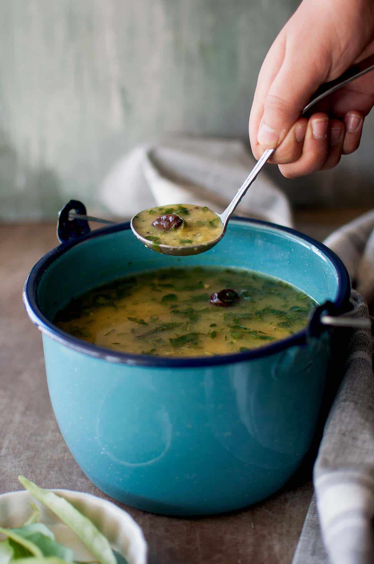 Hand holding a spoon with dal rasam