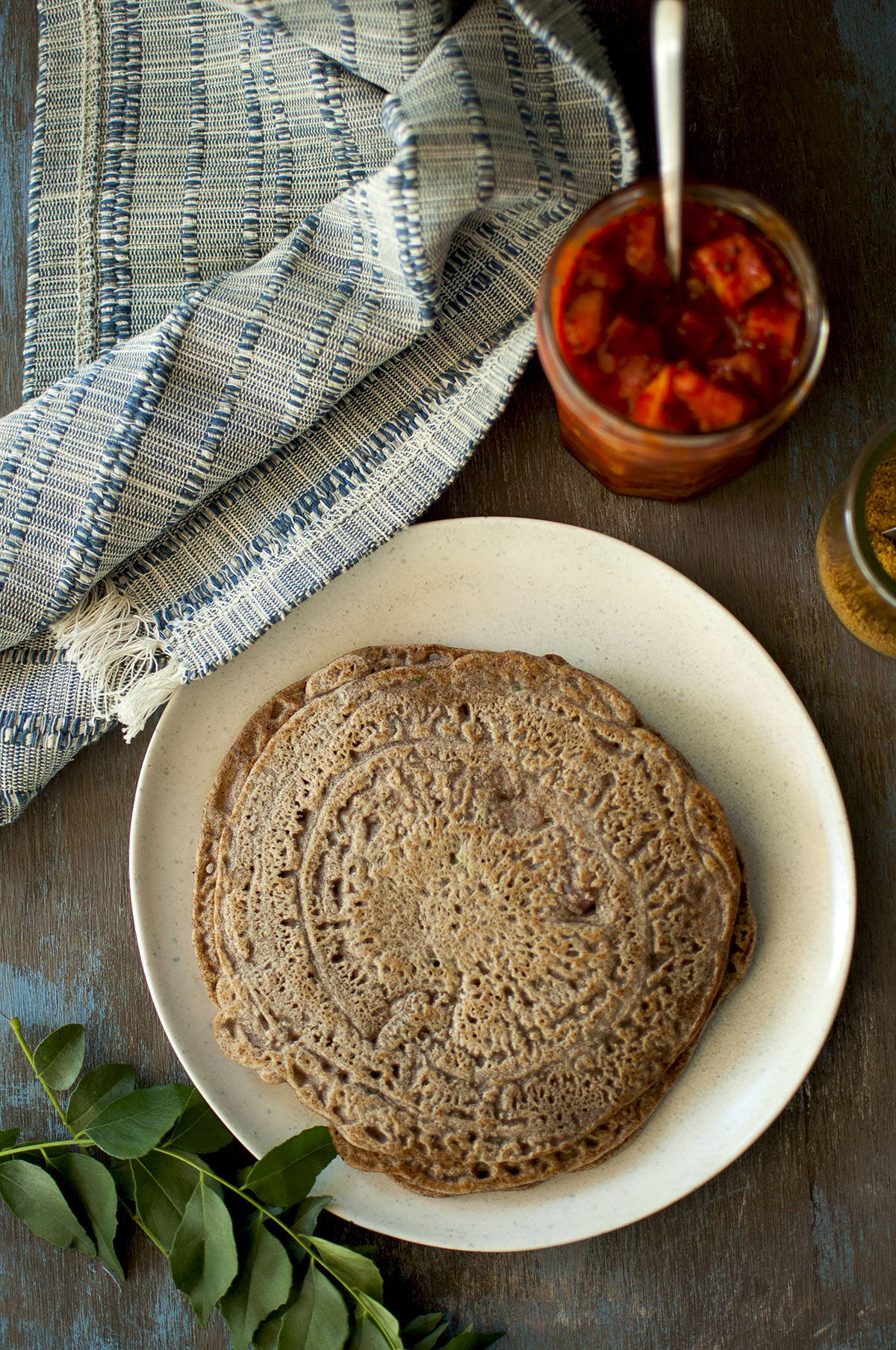 White plate with ragi adai and a jar of mango pickle on the side