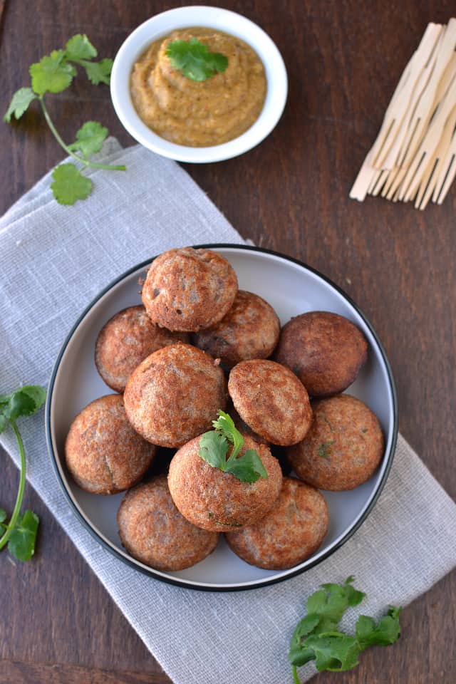Black and white plate with ragi paniyaram topped with cilantro and served with chutney
