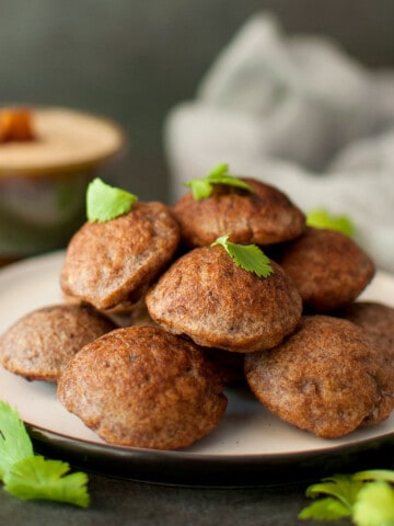 Grey plate with stack of ragi paniyaram topped with cilantro.