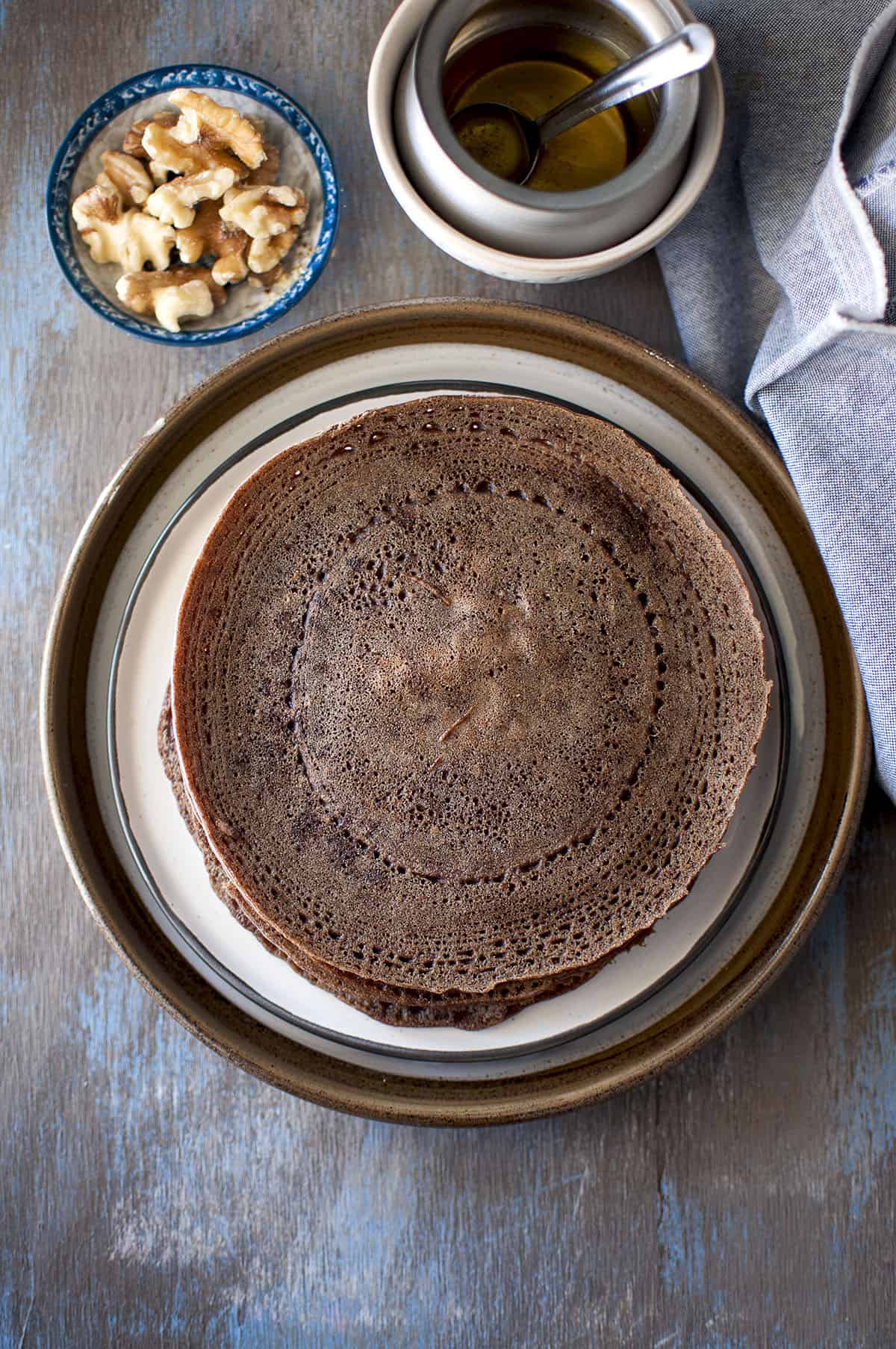 Brown plate with a stack of millet crepes with ghee and wanuts in the background