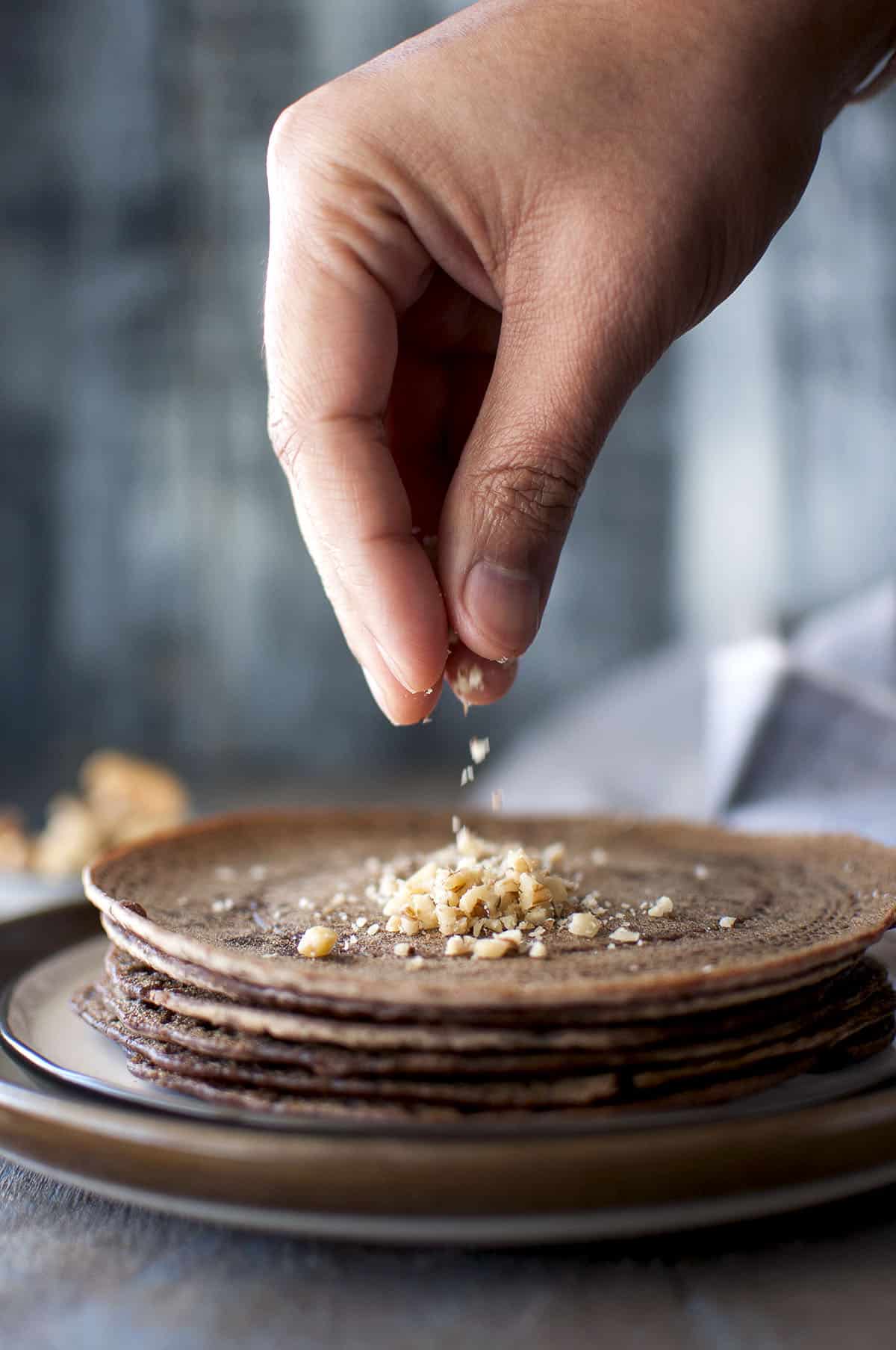 Hand sprinkling chopped walnuts on a stack of adai