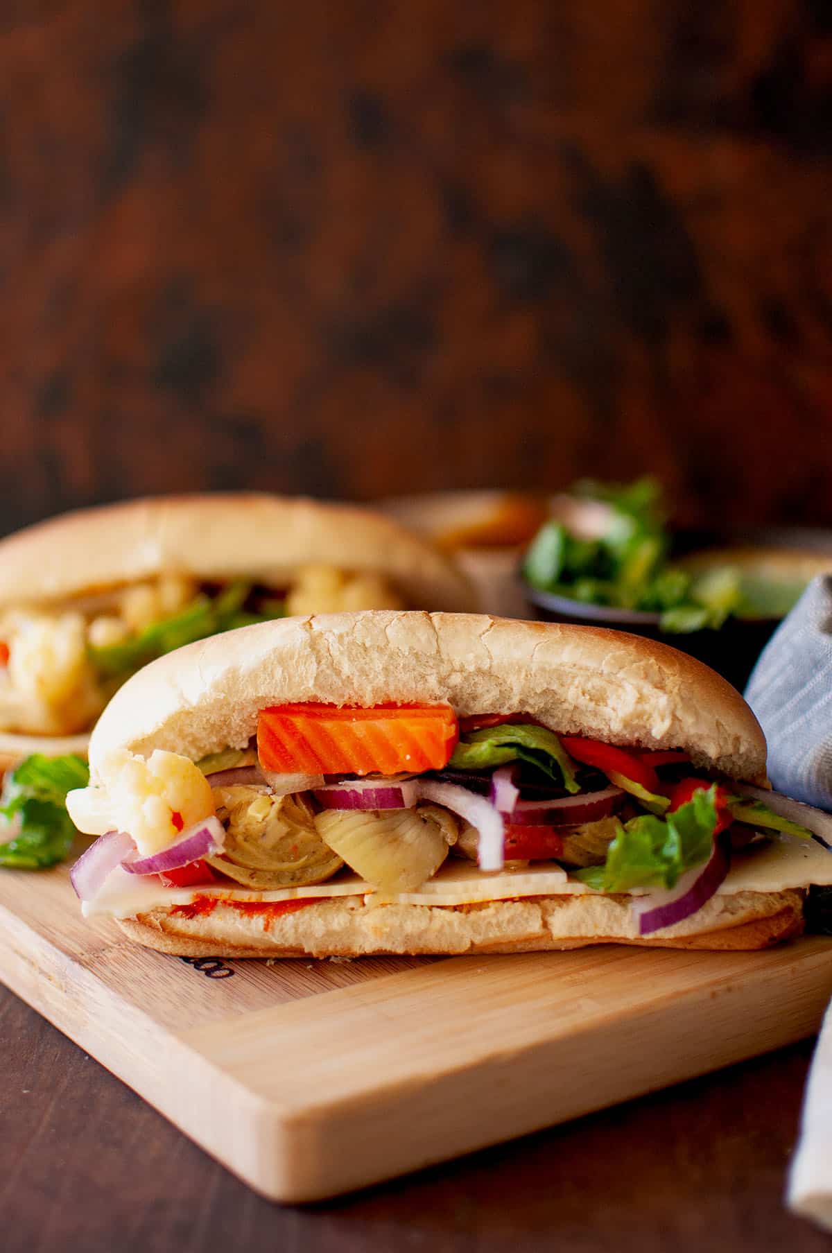 Chopping board with veggie hoagie sandwich.