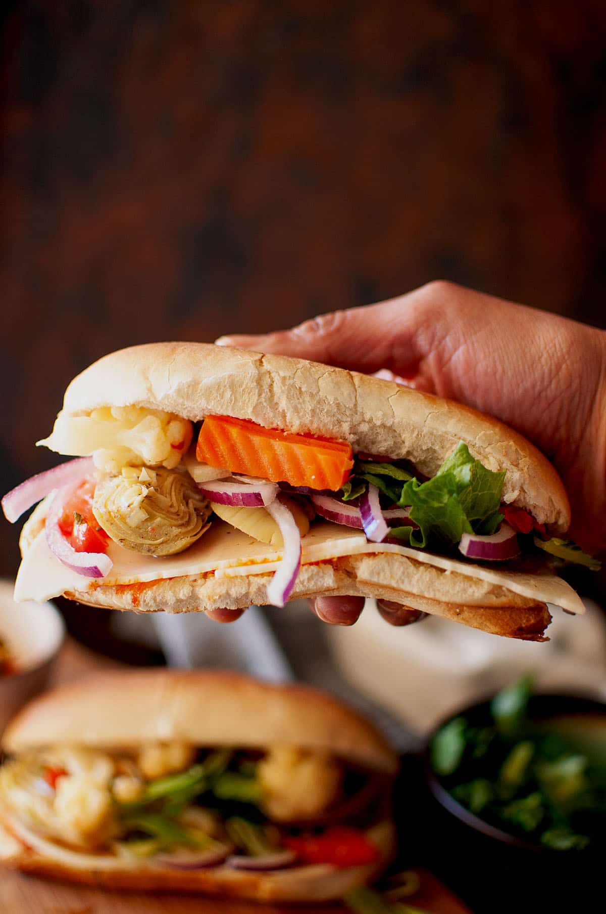 Hand holding a vegetarian hoagie sandwich.