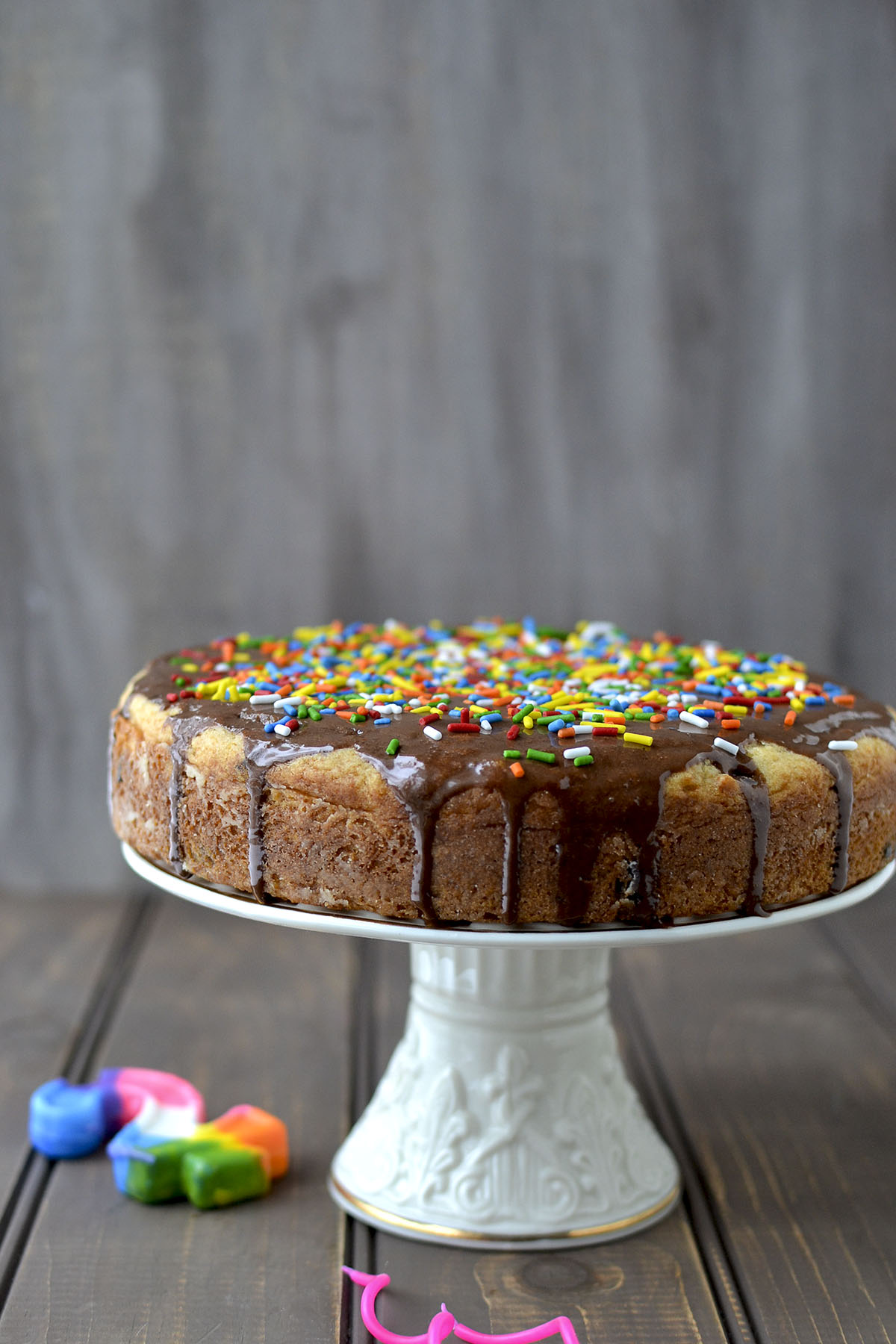 White Cake Stand with eggless vanilla cake drizzled with chocolate ganache and sprinkles on top