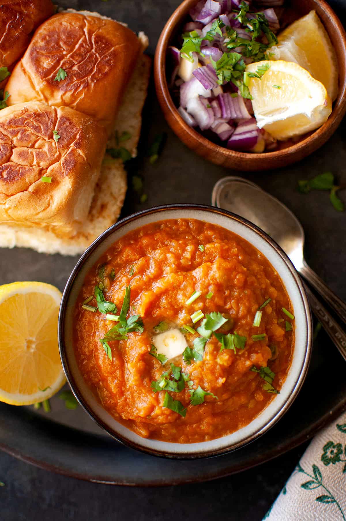 Top view of a tray with bowl of bhaji and toasted buns.