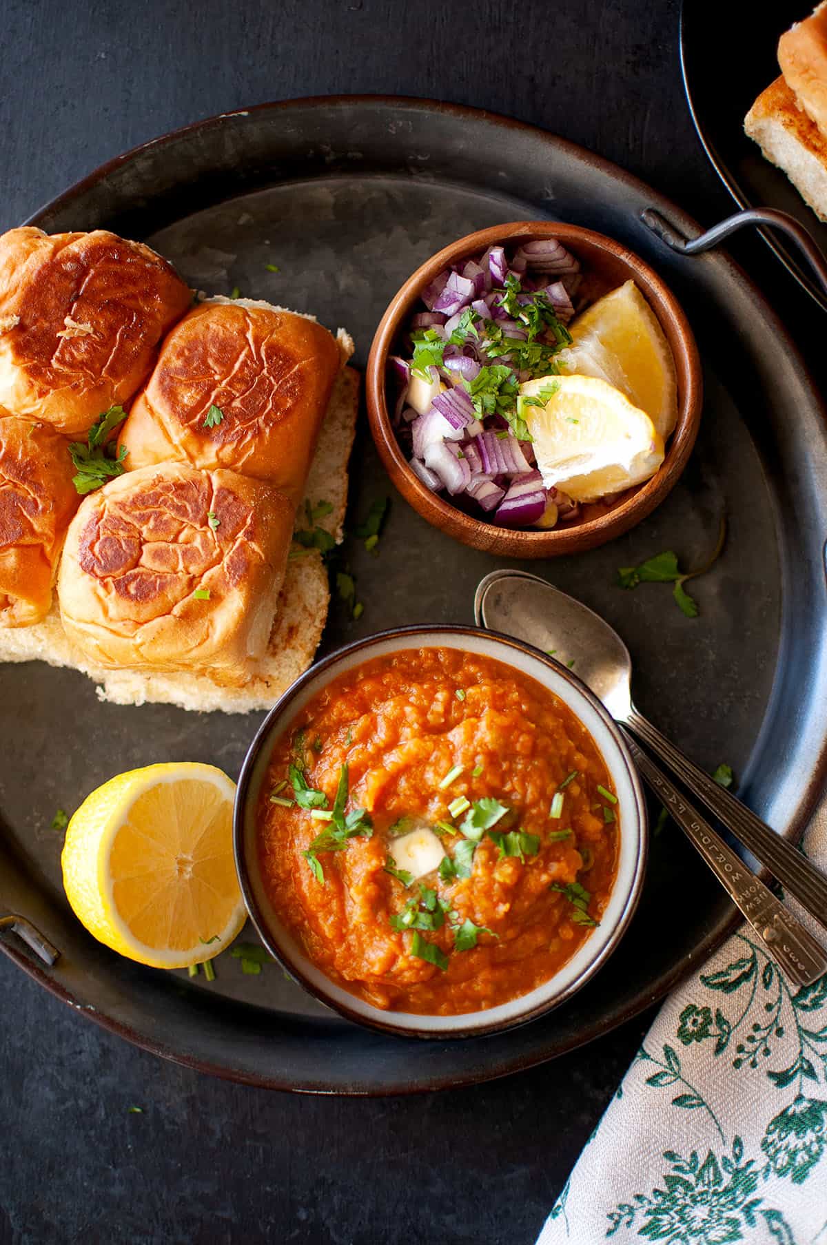 Tray with a bowl of bhaji, toasted buns, chopped onion and lemon wedges.