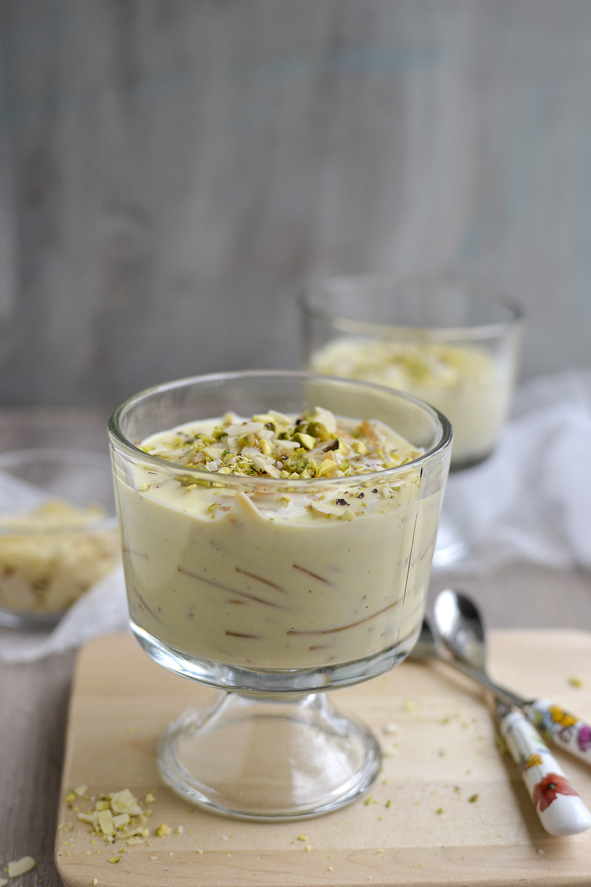 Glass serving cup with creamy noodle pudding topped with chopped almonds and pistachios