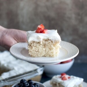 Hand holding white plate with vegan Tres Leche cake