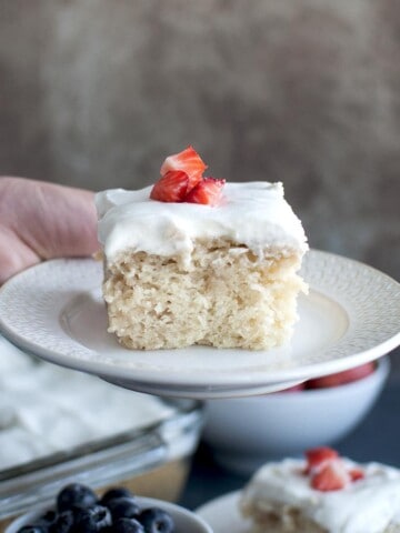 Hand holding white plate with vegan Tres Leche cake