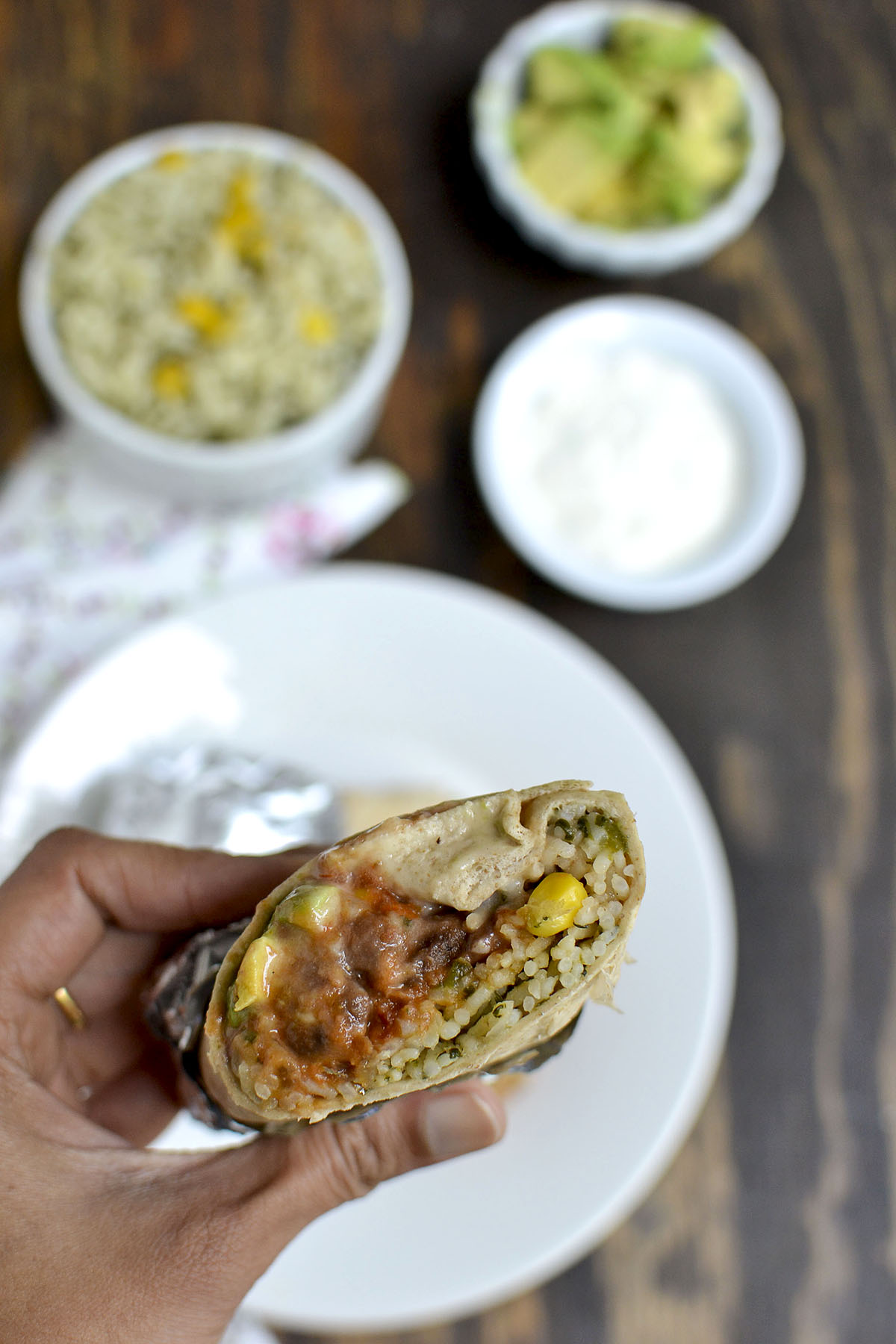 Hand holding half a burrito with rice, corn and cheese