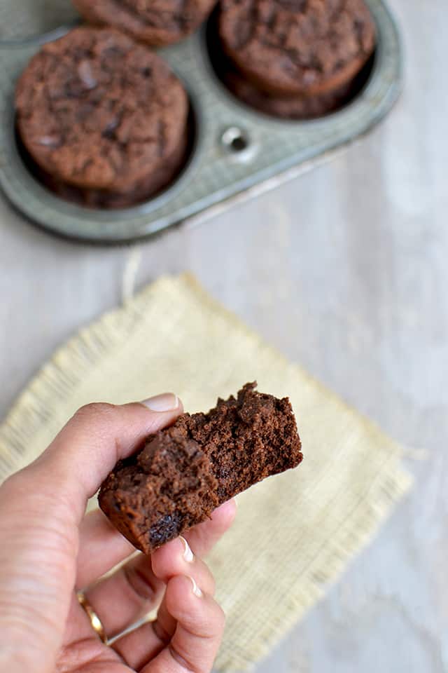 Fingers holding bitten chocolate muffin