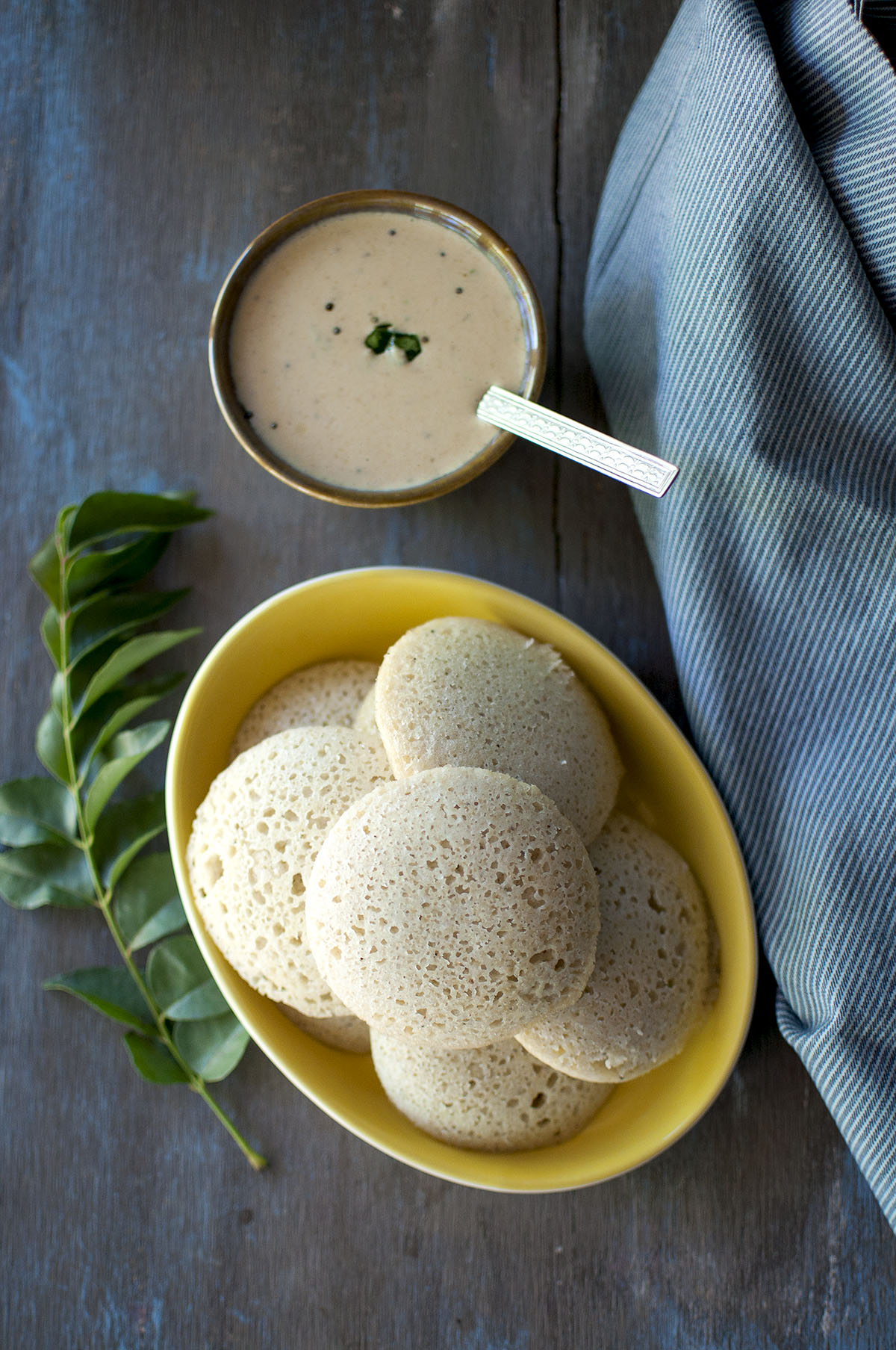 Yellow plate with stack of jowar idli and peanut chutney in the background