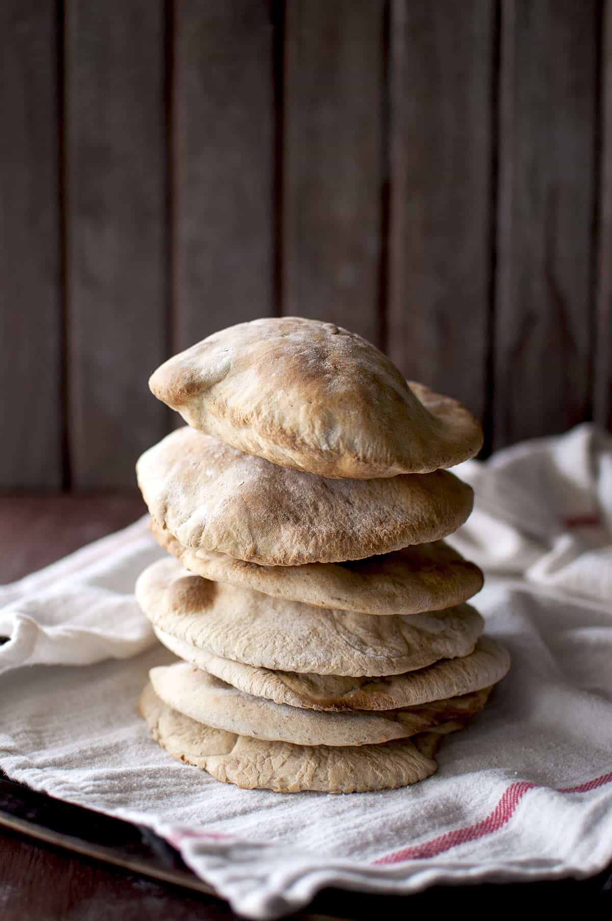 Baking sheet with kitchen towel with a stack of puffy Khobez bread