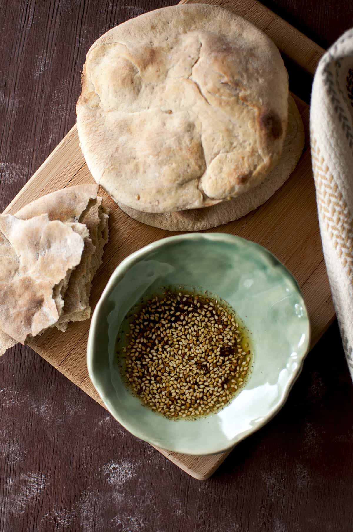 Chopping board with Khobez and a green bowl with za'atar olive oil