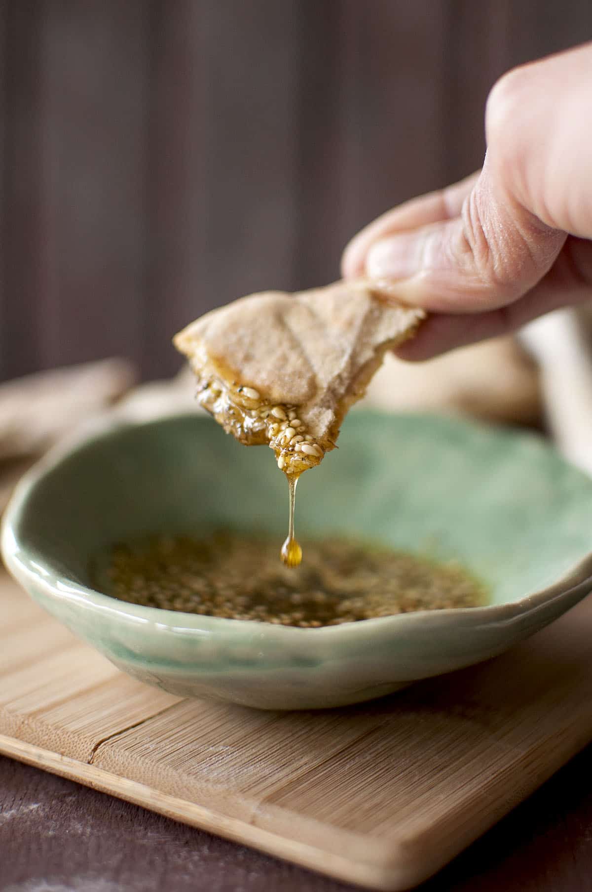 Hand holding a piece of khobez with oil dripping into a green bowl