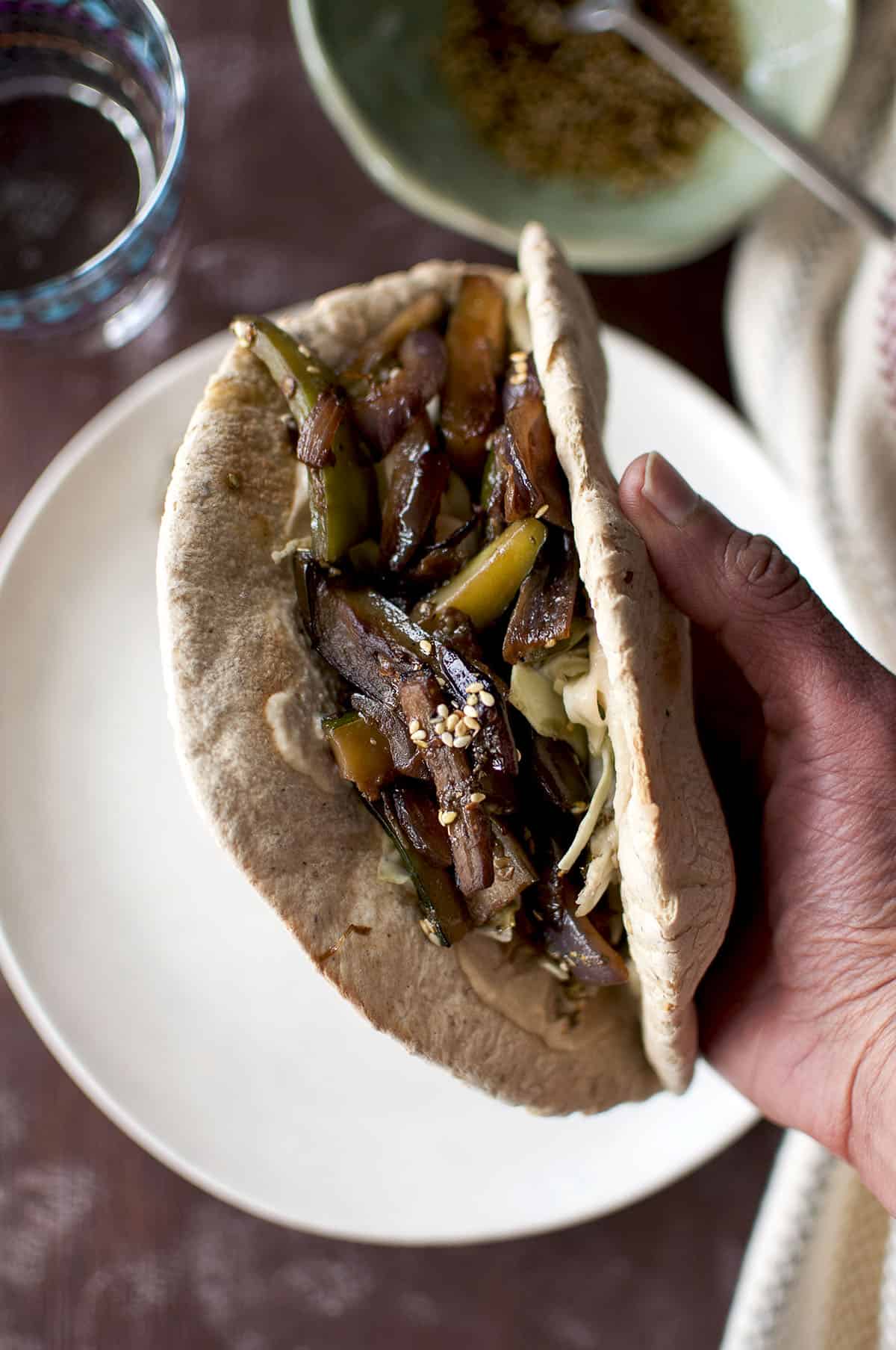 Hand holding a sandwich wrap with roasted veggies