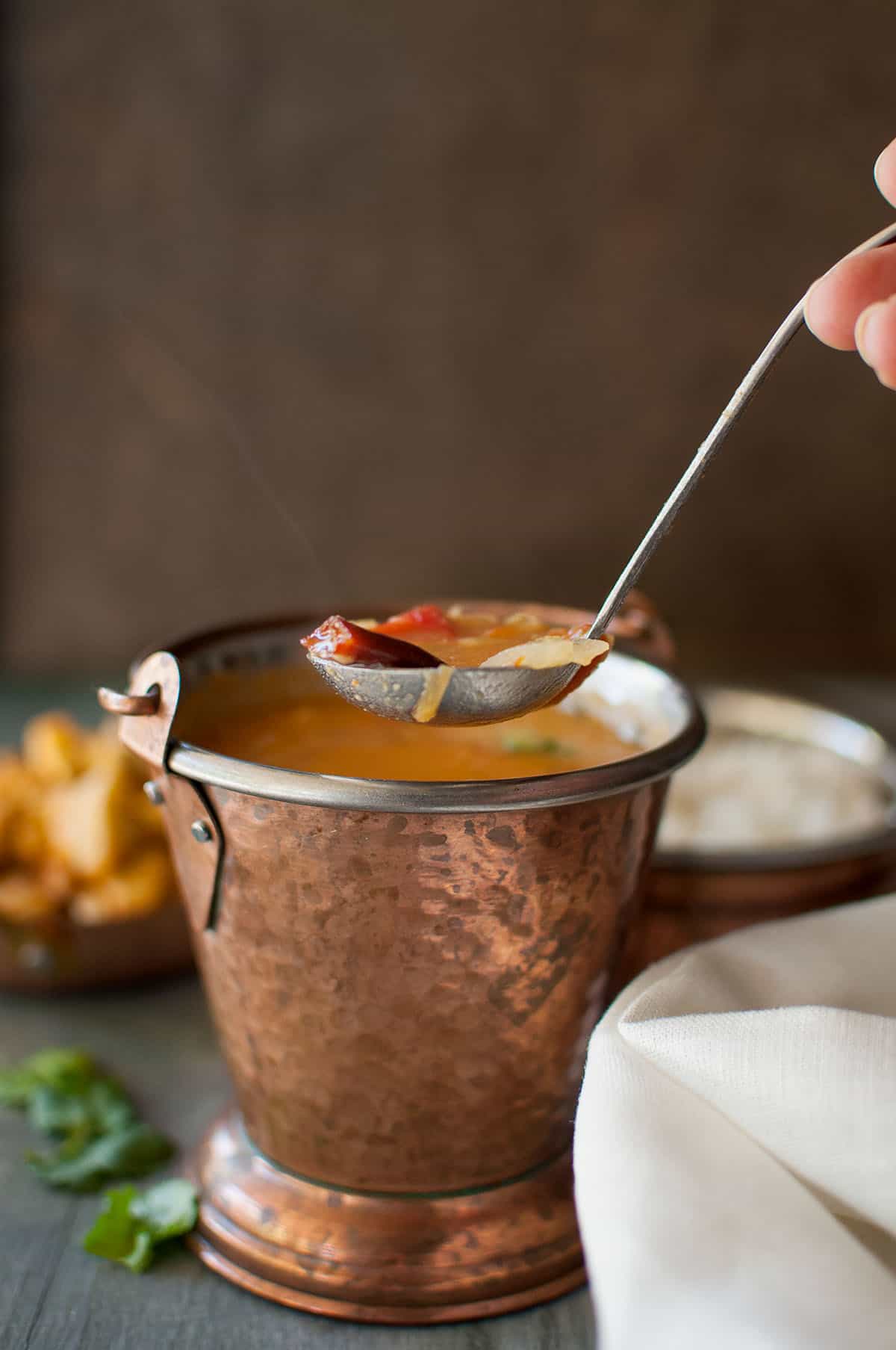 Hand holding a spoon with Saravana bhavan sambar.