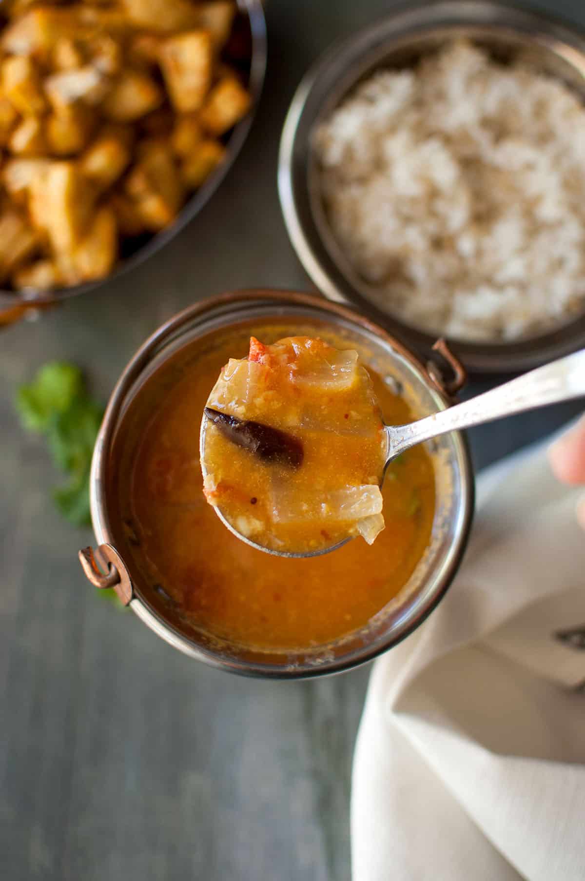 Spoon holding vegetable stew over a bowl.