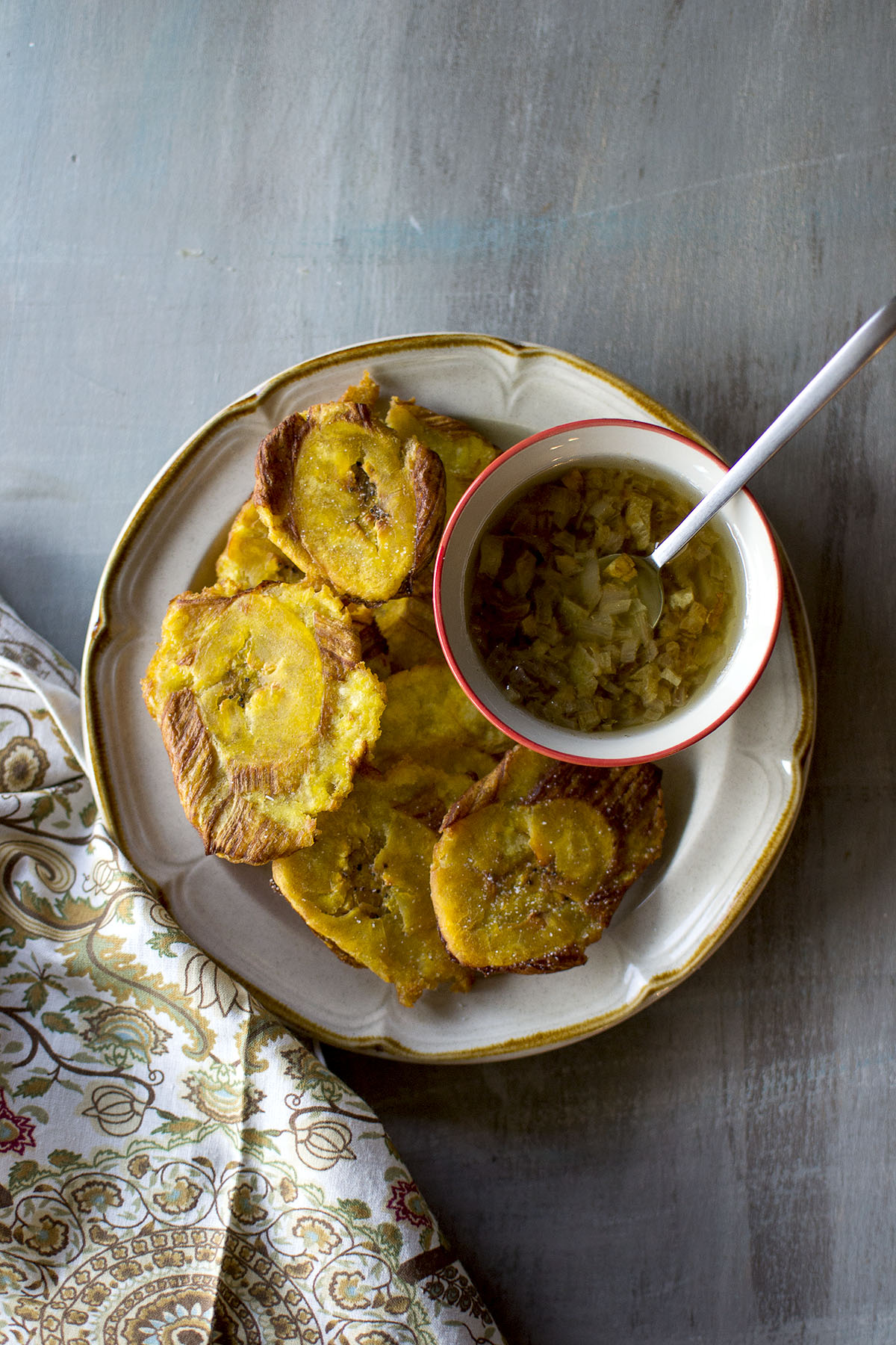 Grey plate with Cuban tostones and a bowl of mojo sauce.