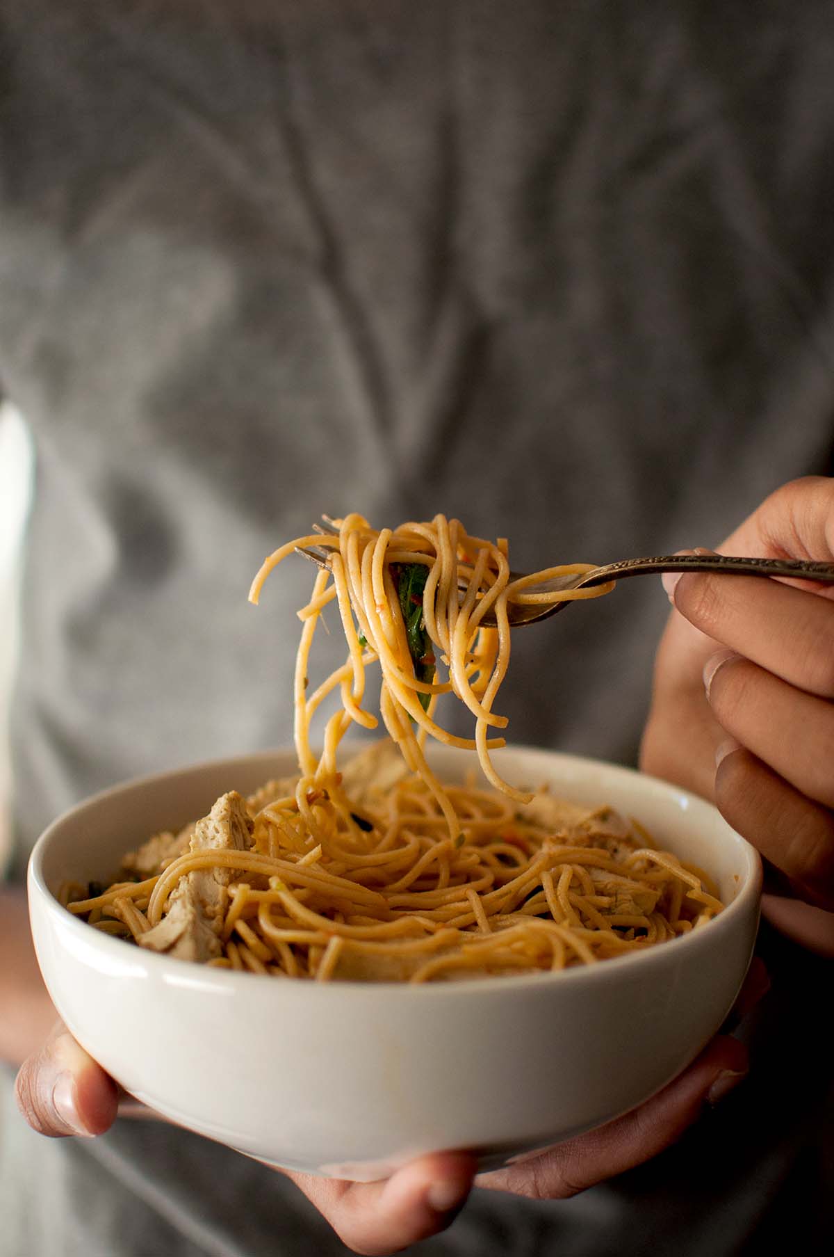 Person holding a white bowl and a fork with spaghetti.