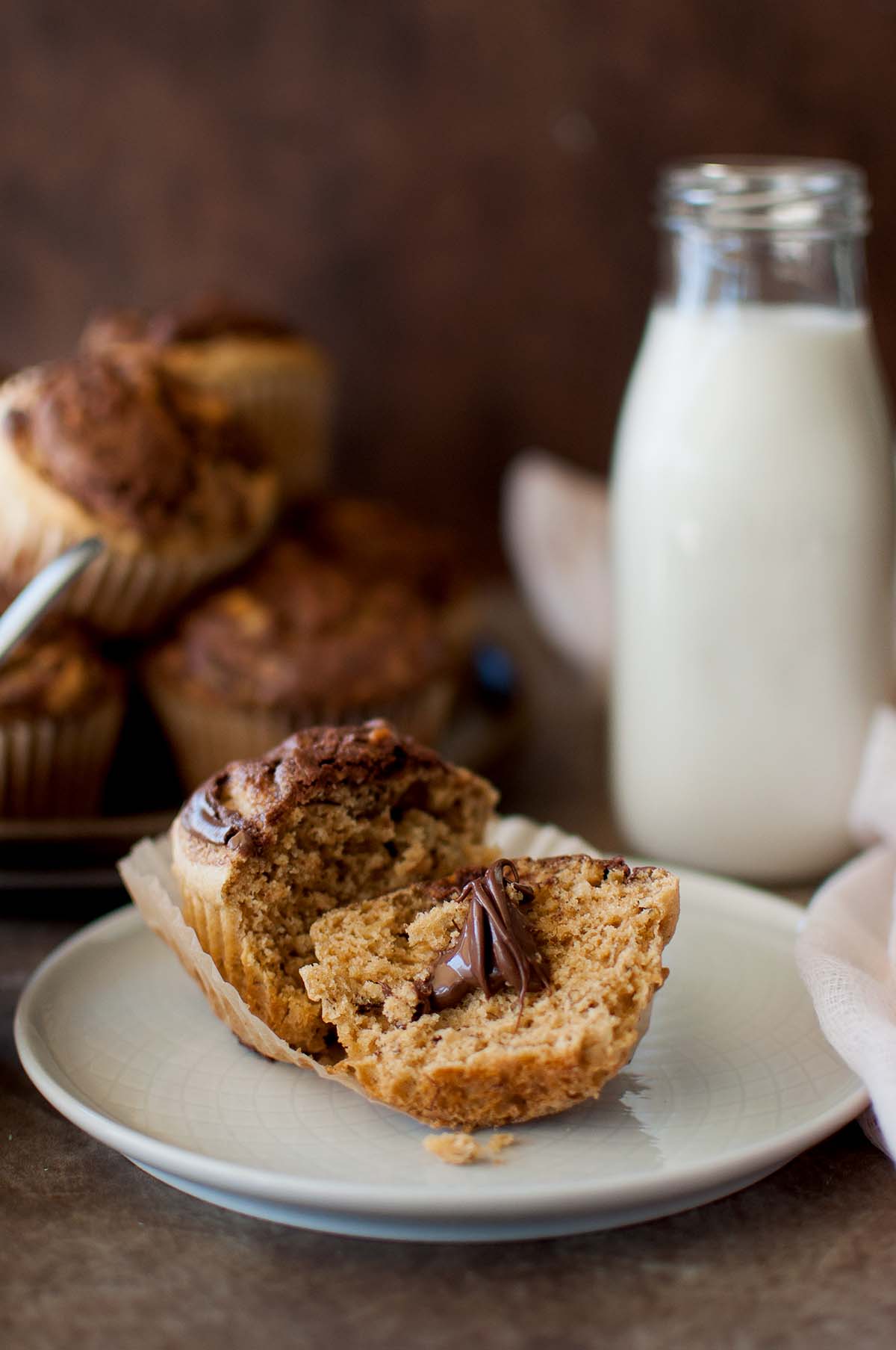 White plate with halved muffin topped with Nutella and a glass jar of milk in the background.