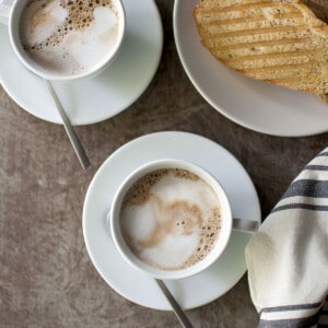 Two white cups with espresso and toast in the background