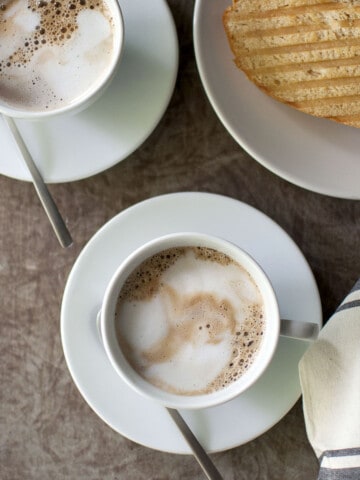 Two white cups with espresso and toast in the background