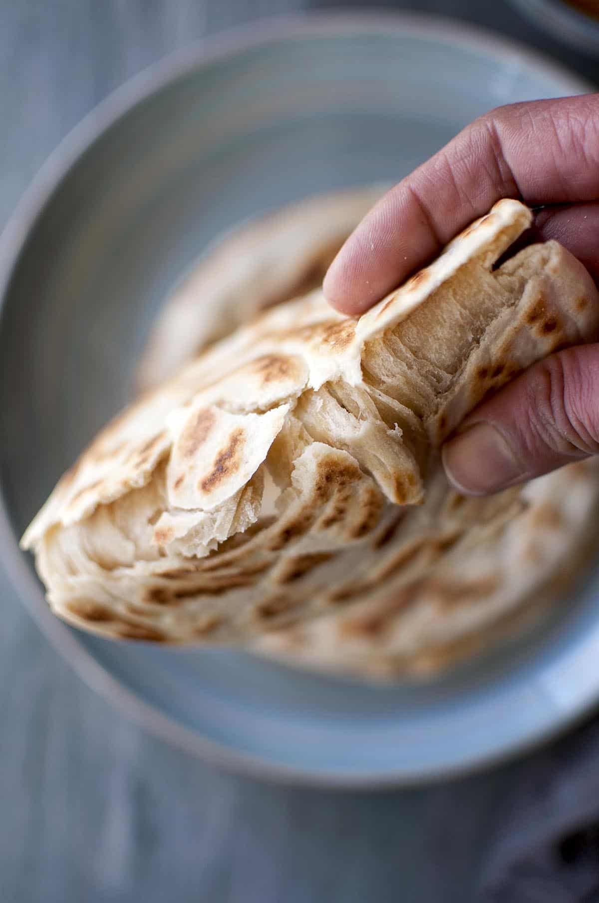 hand holding flaky Malaysian roti canai