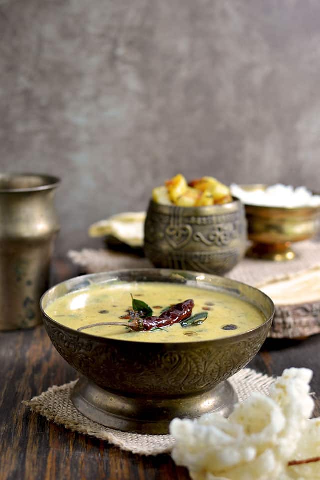 Bowl of Mor Kuzhambu with potato curry and crispies