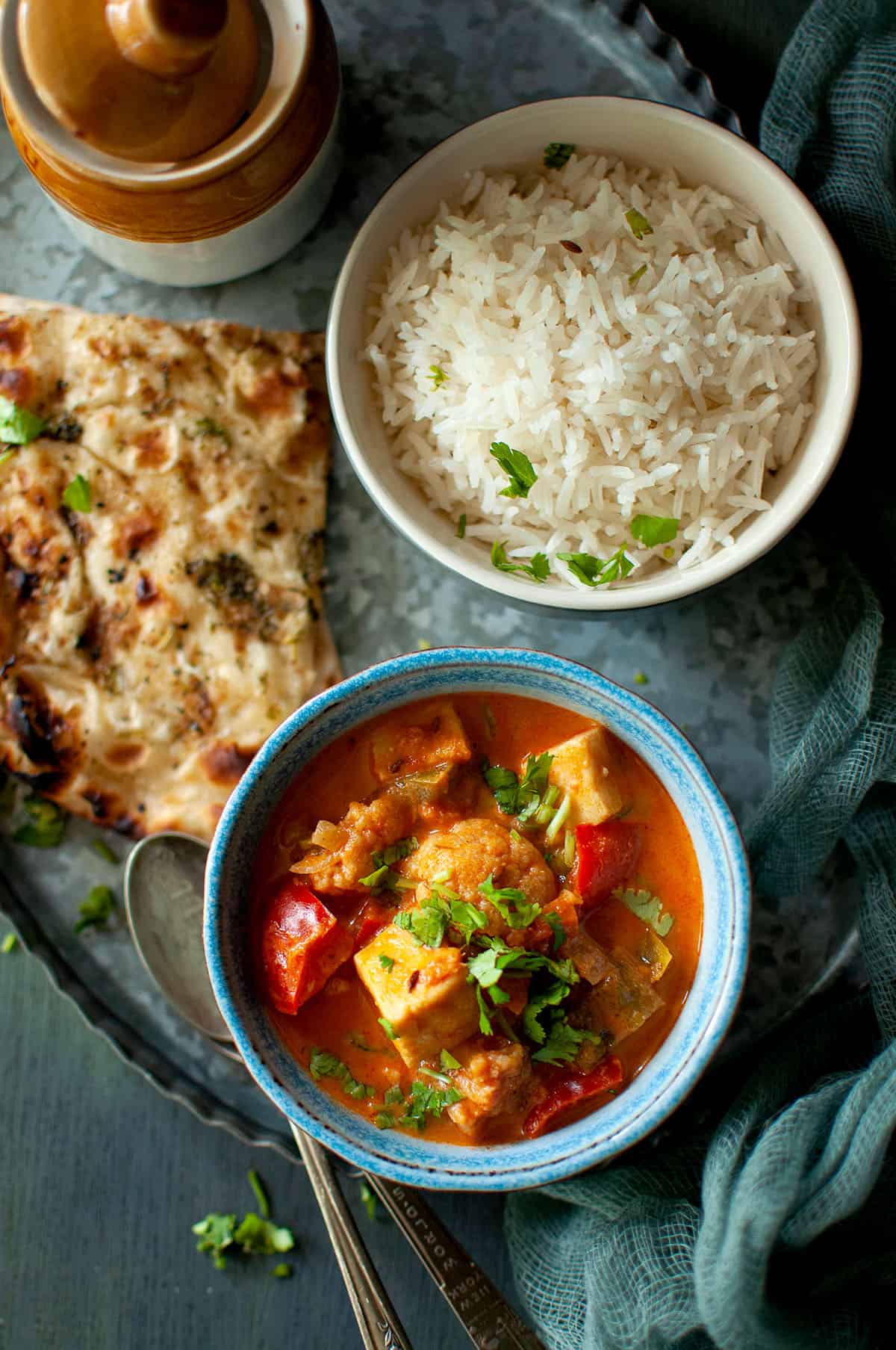 Blue bowl with shahi paneer korma and naan, rice and pickle in the back.