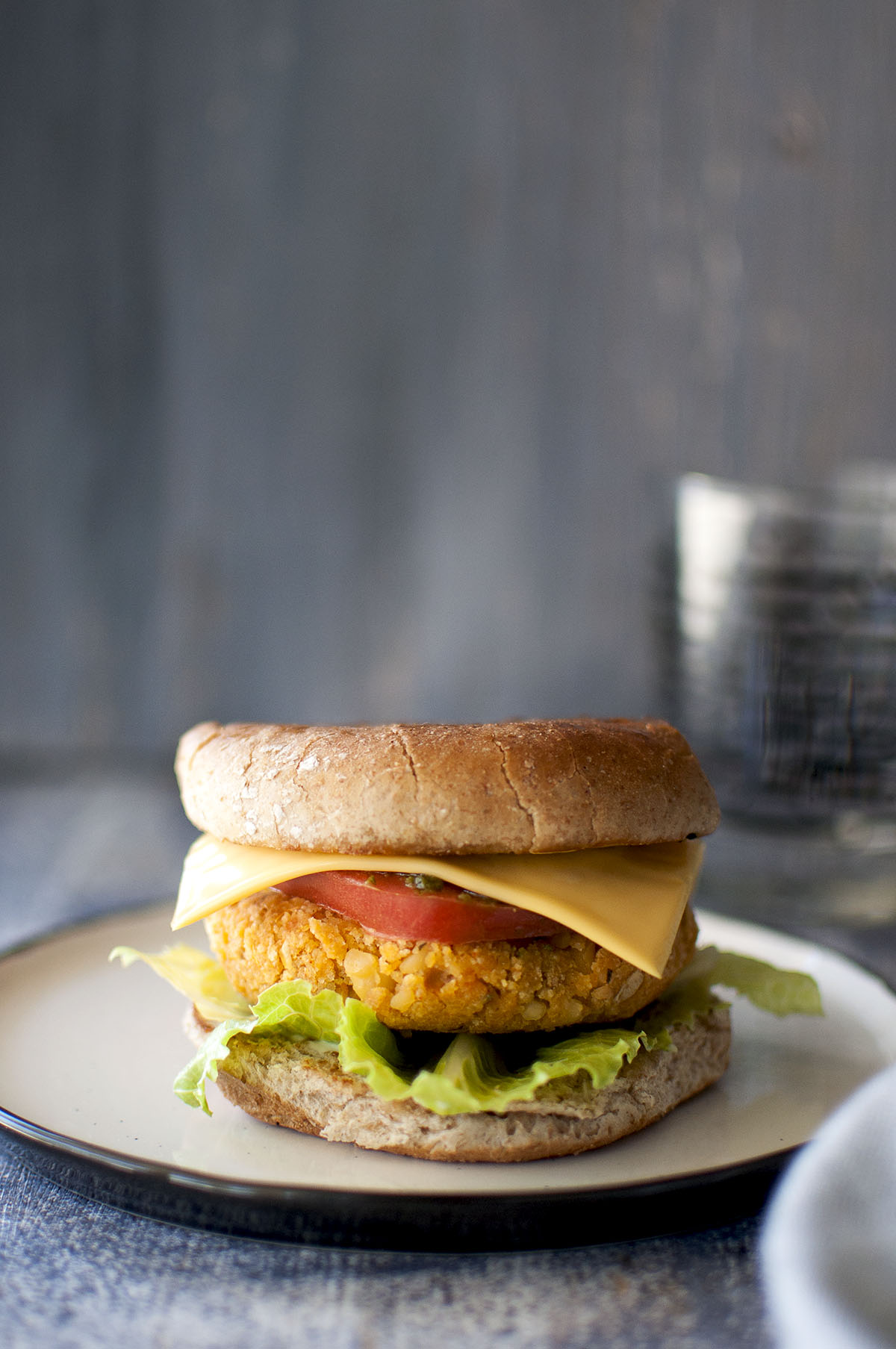 White plate with Sweet potato chickpea burger sandwich with lettuce, tomato and cheese