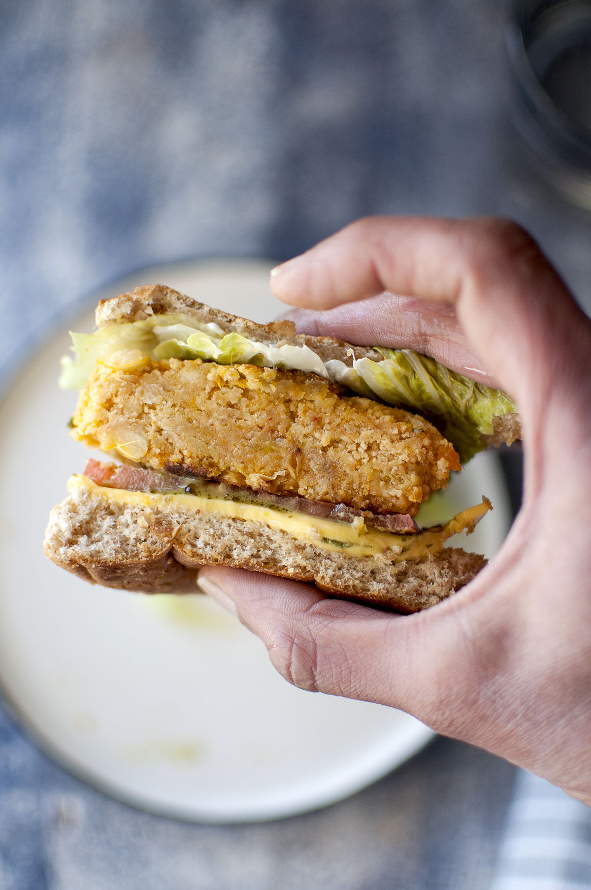 Hand holding a burger sandwich with veggie patty, cheese slice, lettuce and tomato slice