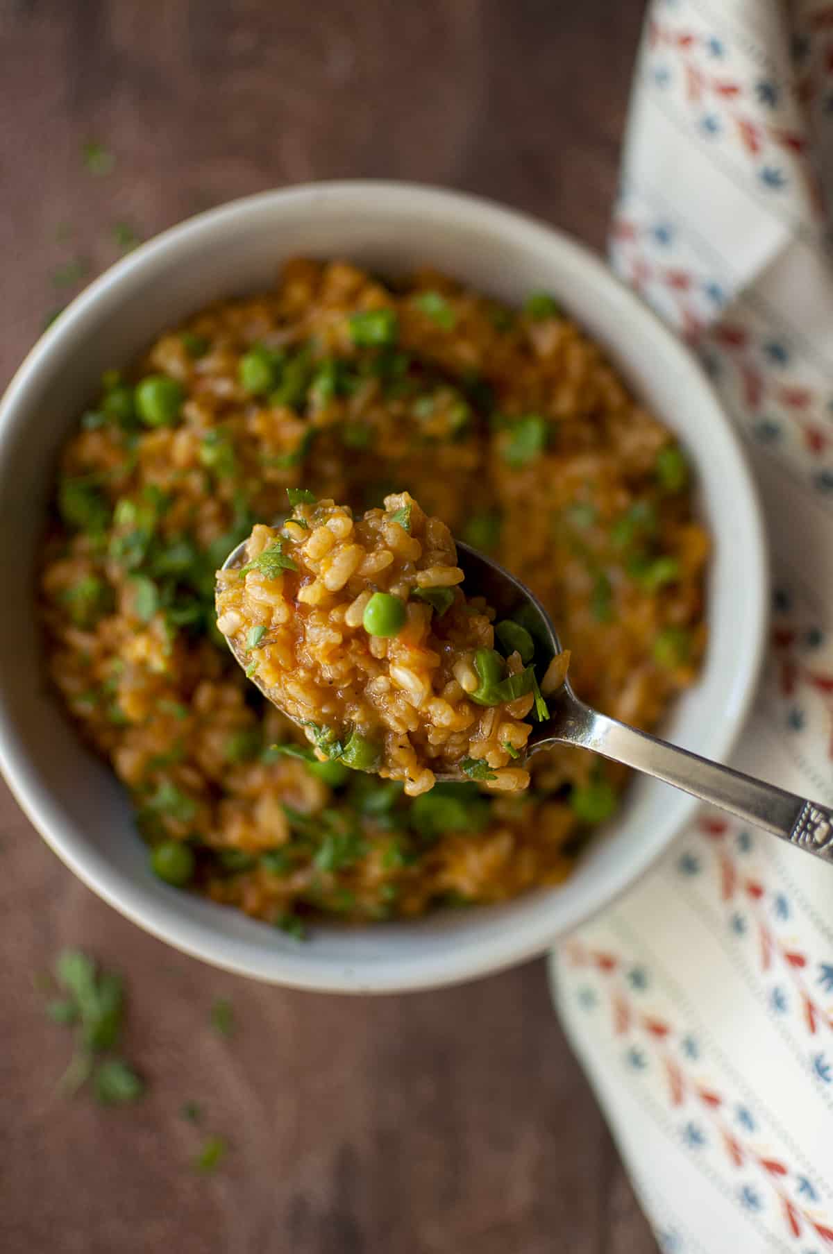 Steel spoon with African tomato rice and a bowl of rice in the background