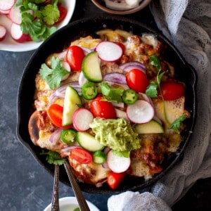 Cast iron skillet with Indian nachos topped with fresh veggies.