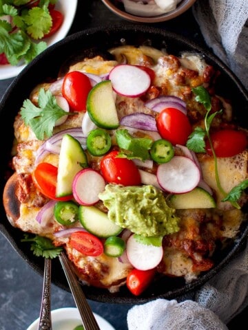 Cast iron skillet with Indian nachos topped with fresh veggies.