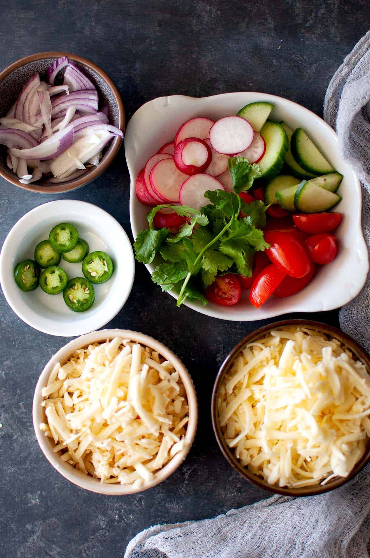 Bowls with fresh veggies, grated cheese, onions and jalapeno peppers.