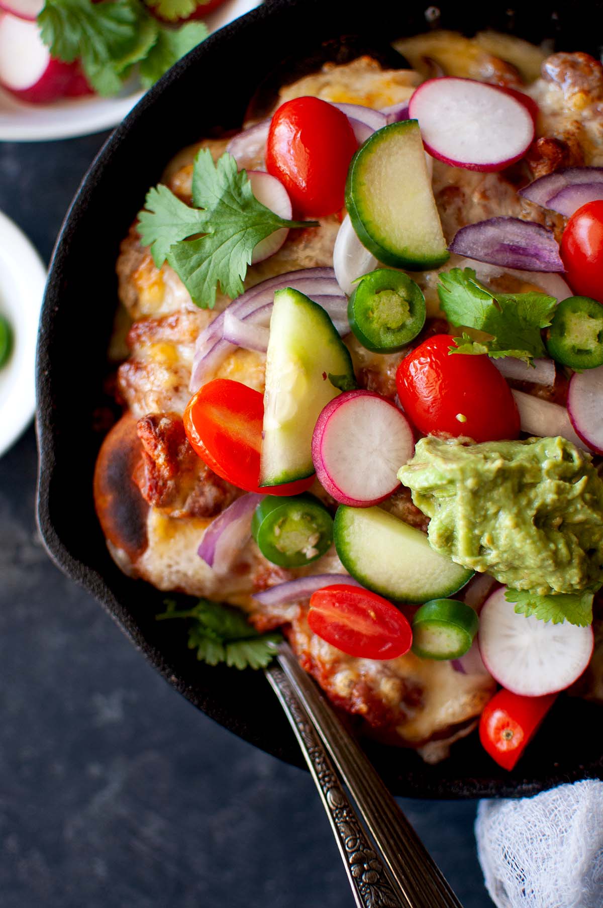 Cast iron skillet with Indian nachos topped with fresh veggies.