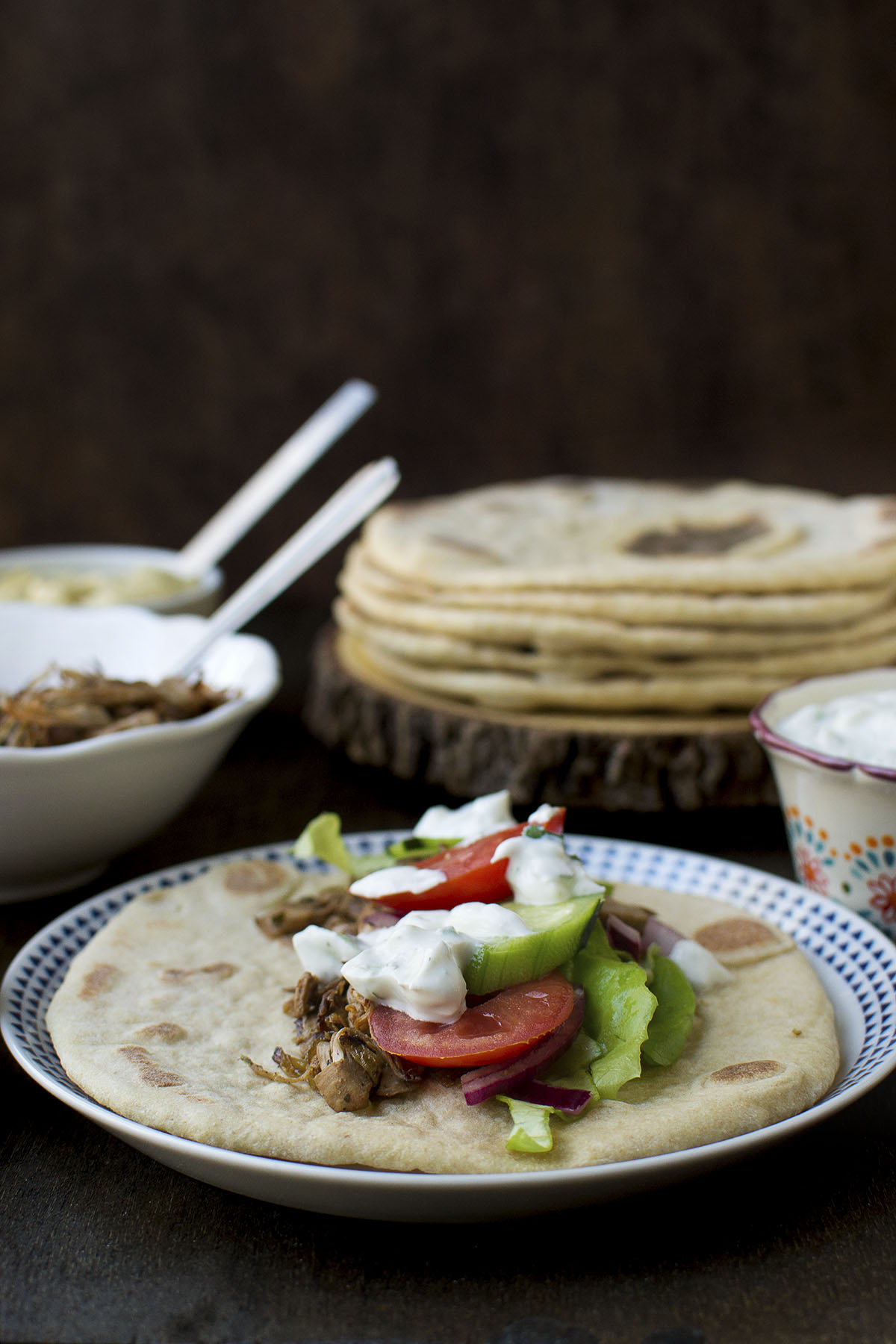 White plate with pita topped with jackfruit stuffing, veggies and yogurt