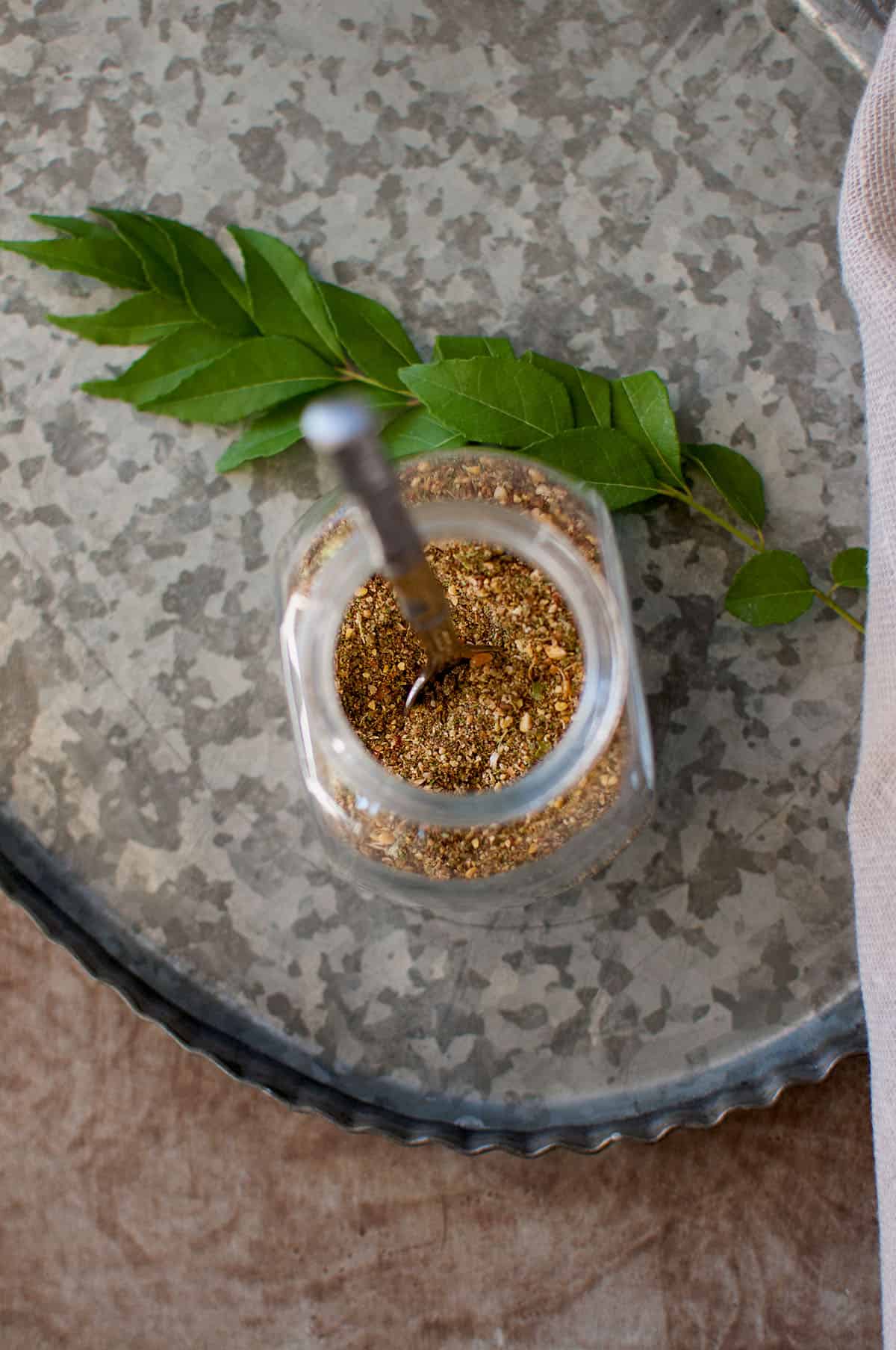 Tray with a glass jar of curry leaf powder and a curry leaves sprig in the back.