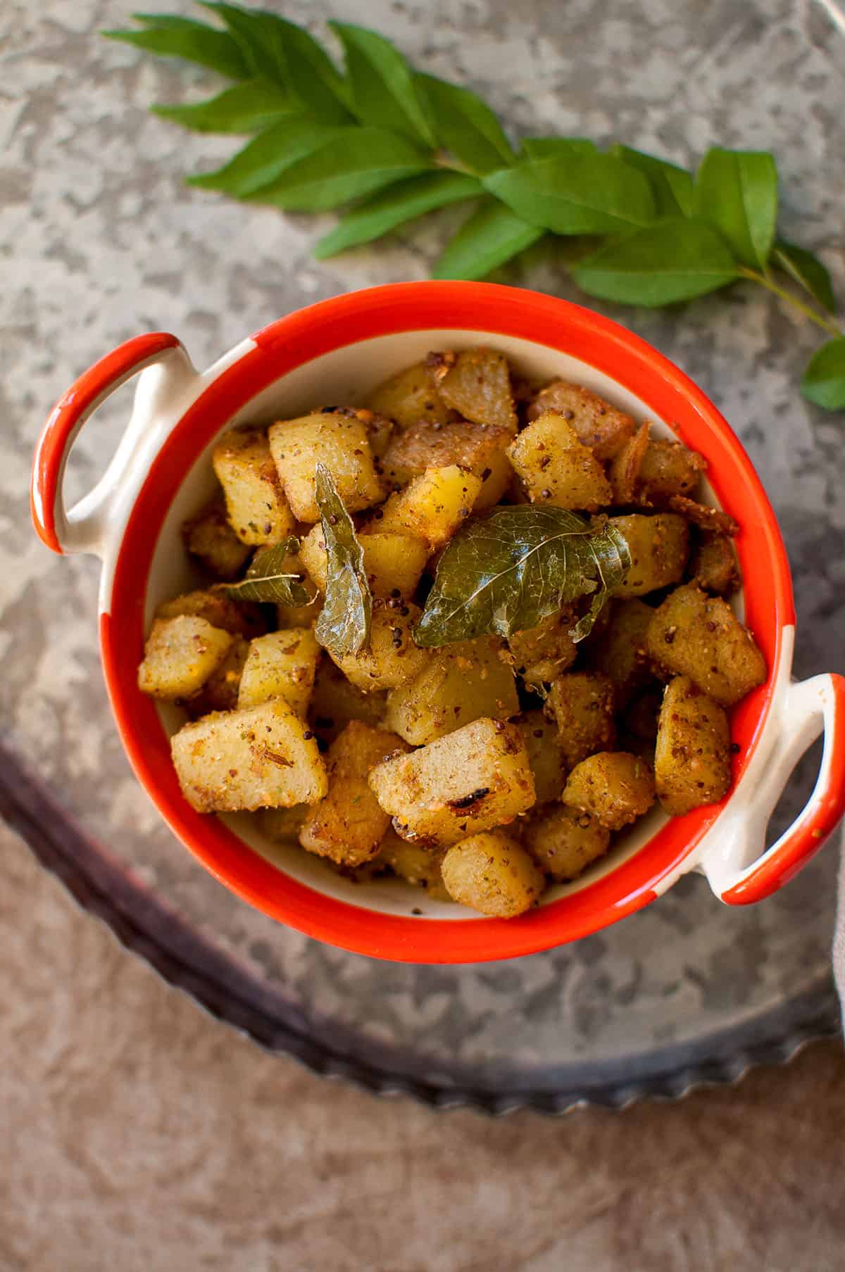 Top view of orange bowl with dry potato curry.